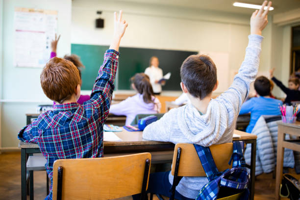 Schoolchildren at classroom with raised hands answering teacher's question.