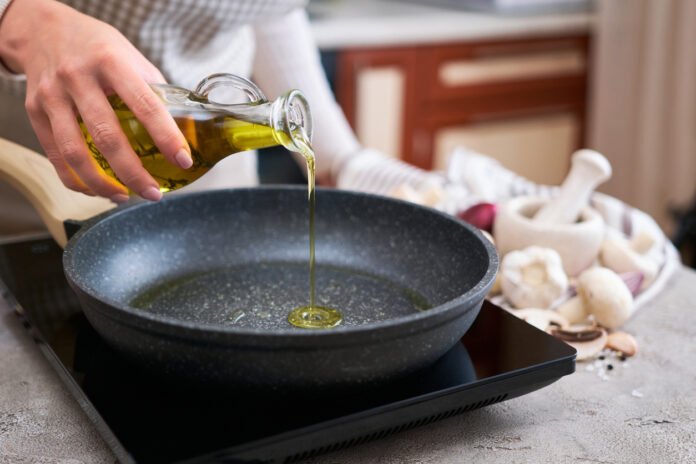Woman pouring olive oil on frying pan at domestic kitchen